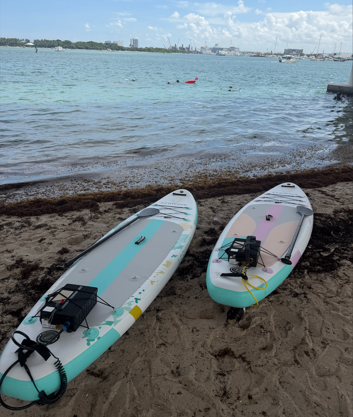 Two AerWave boards resting on a sandy beach beside a turquoise bay